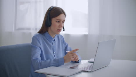 female-specialist-of-call-center-is-talking-by-headset-and-looking-at-display-of-laptop-portrait-indoors-working-remotely